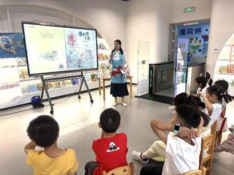 说明: 图2:陈老师穿上亲手制作的故事衣,将著名作家高洪波的绘本《图书馆之夜》向小读者们娓娓道来。孩子们听得津津有味。